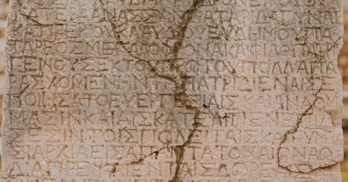 Close-up of a weathered stone with ancient Greek letters inscribed, showcasing historical text.